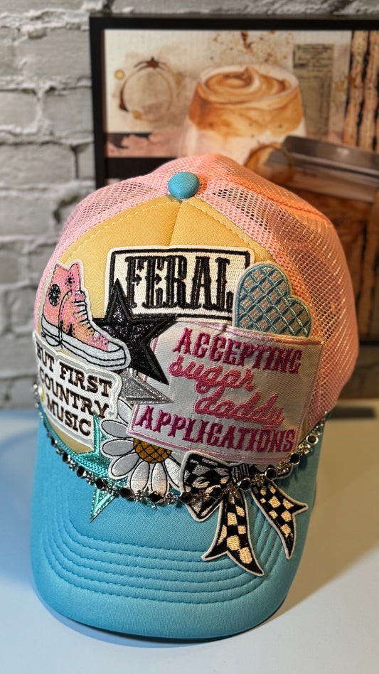 Colorful cap with patches and text on a light blue base, against a brick wall background.