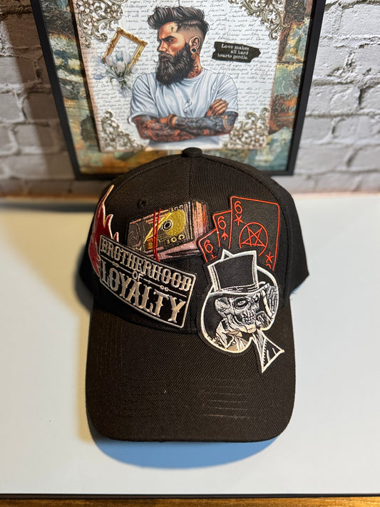 Black cap with embroidered designs on a white surface with a framed picture in the background.